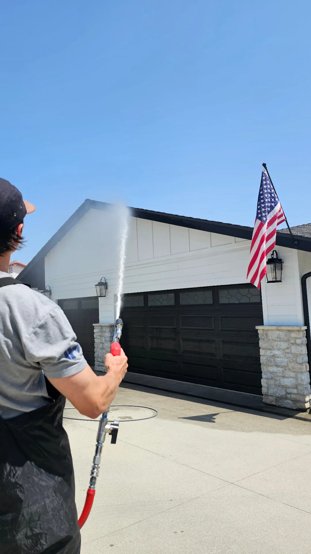 Technician applying a low-pressure soft wash treatment to a residential exterior