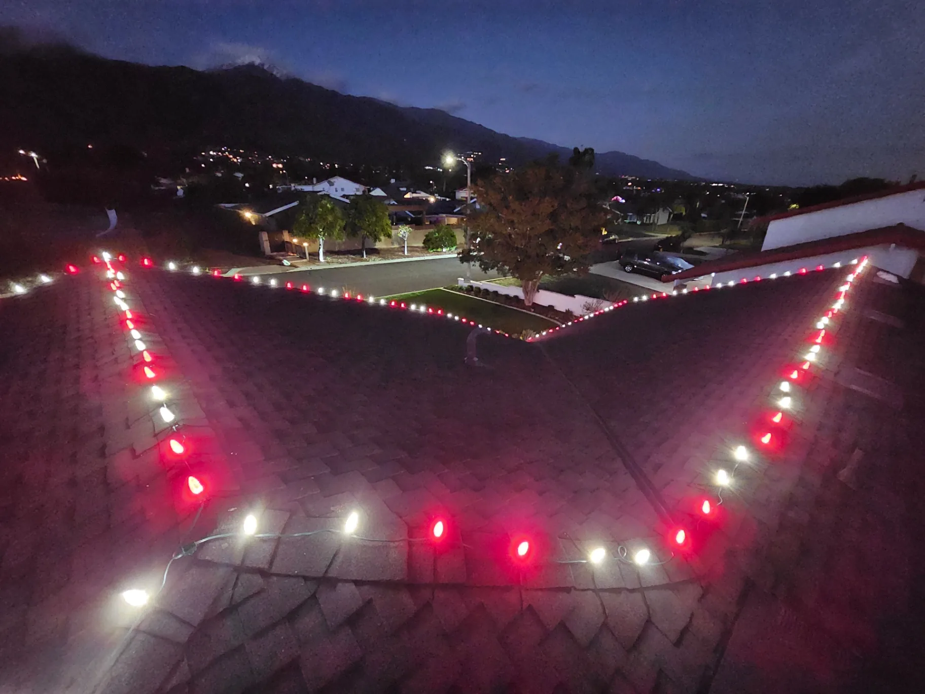 Aerial dusk view of crisp red and white holiday lights tracing every roofline peak of a residential home
