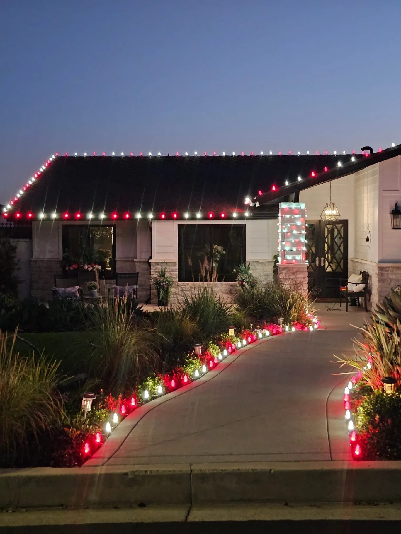 Dusk view of a residential home with professionally installed red and white roofline holiday lights and lit walkway
