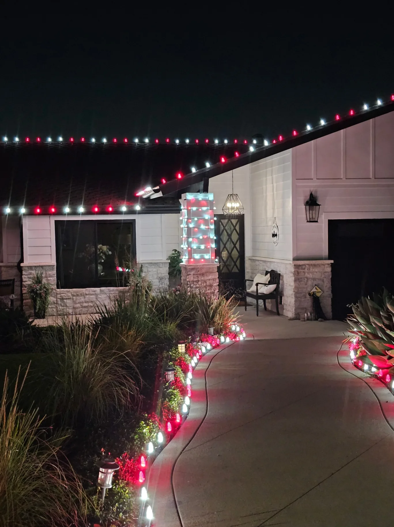 Finished Christmas light display showcasing roofline lights, a wrapped entry column, and pathway lighting at night