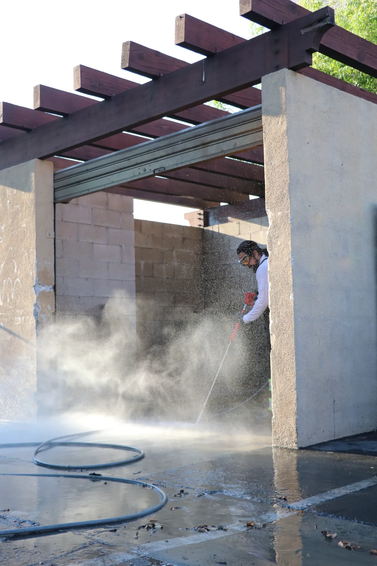 Commercial dumpster pad cleaning in progress under a pergola