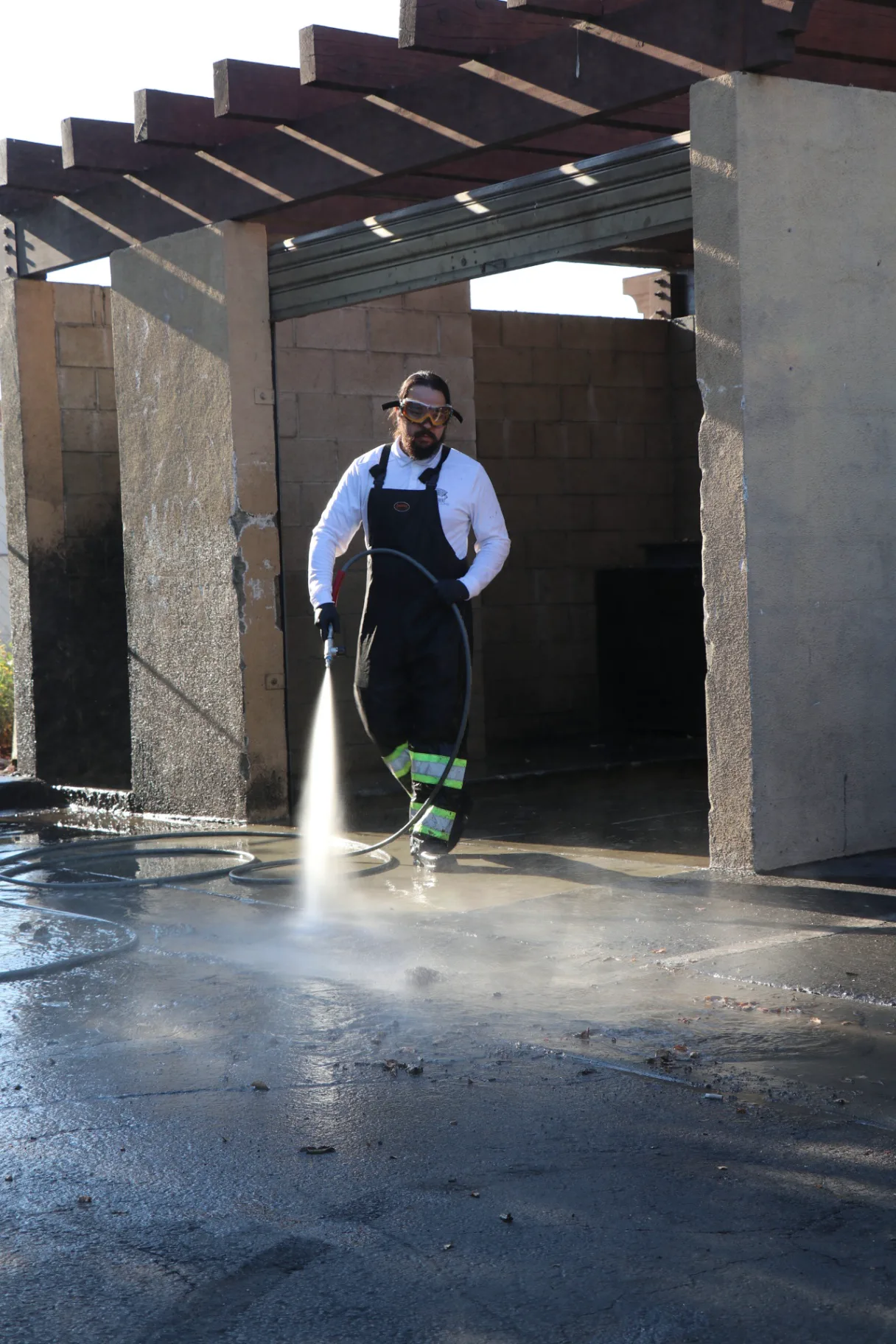 Transparent Solutions technician rinsing a commercial dumpster pad enclosure