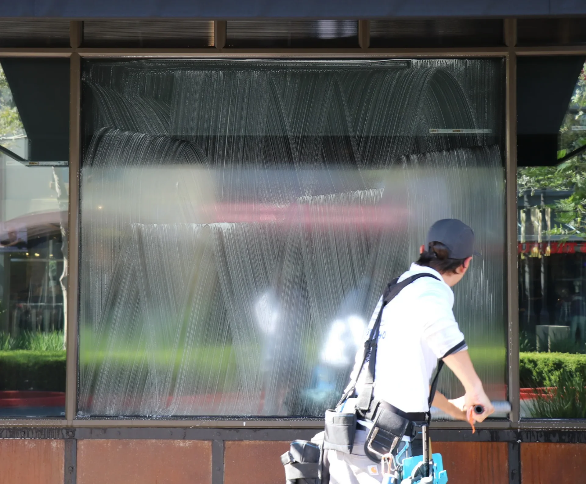 Technician applying soap with a strip washer to a large commercial storefront window