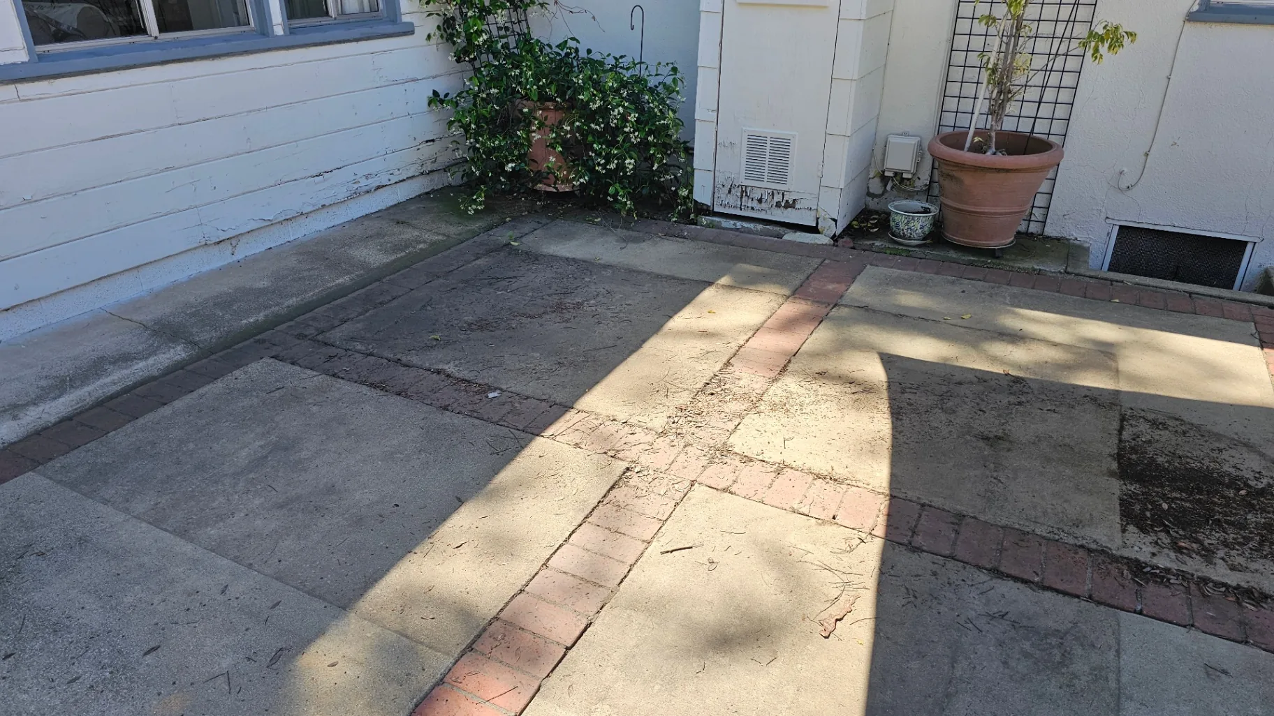 Grimy backyard concrete patio with brick borders before pressure washing