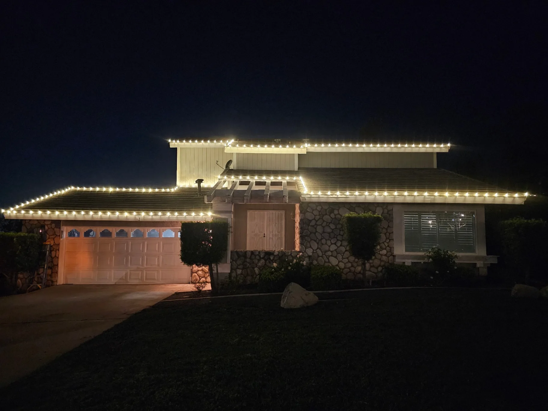 Warm white C9 holiday lights installed cleanly along the rooflines of a two-story home at night